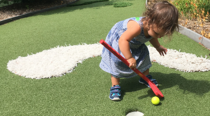 little girl playing mini golf