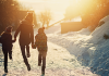 Mom and two kids skipping down snowy trail into the sun.