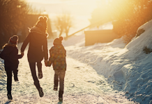 Mom and two kids skipping down snowy trail into the sun.