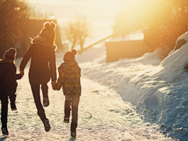 Mom and two kids skipping down snowy trail into the sun.