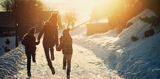 Mom and two kids skipping down snowy trail into the sun.