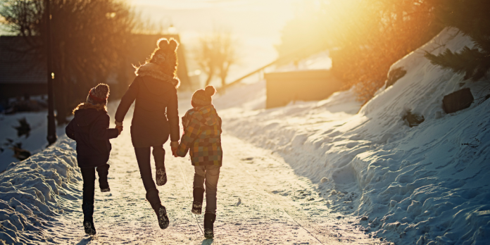 Mom and two kids skipping down snowy trail into the sun.