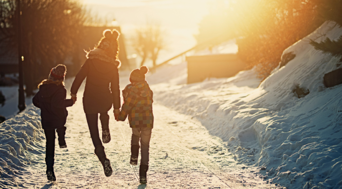 Mom and two kids skipping down snowy trail into the sun.